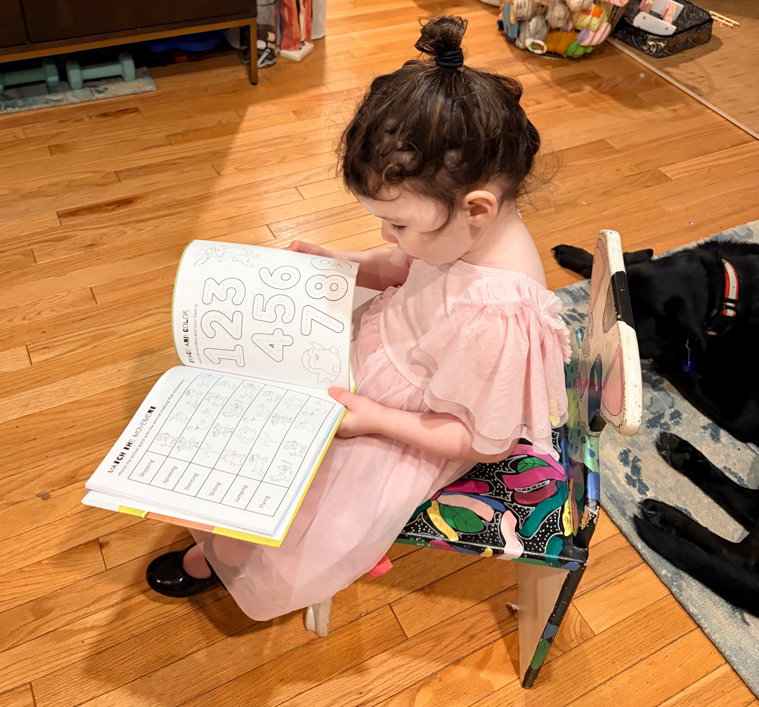 Child sitting on a chair reading a Run, Run, Run! book with numbers on a wooden floor.