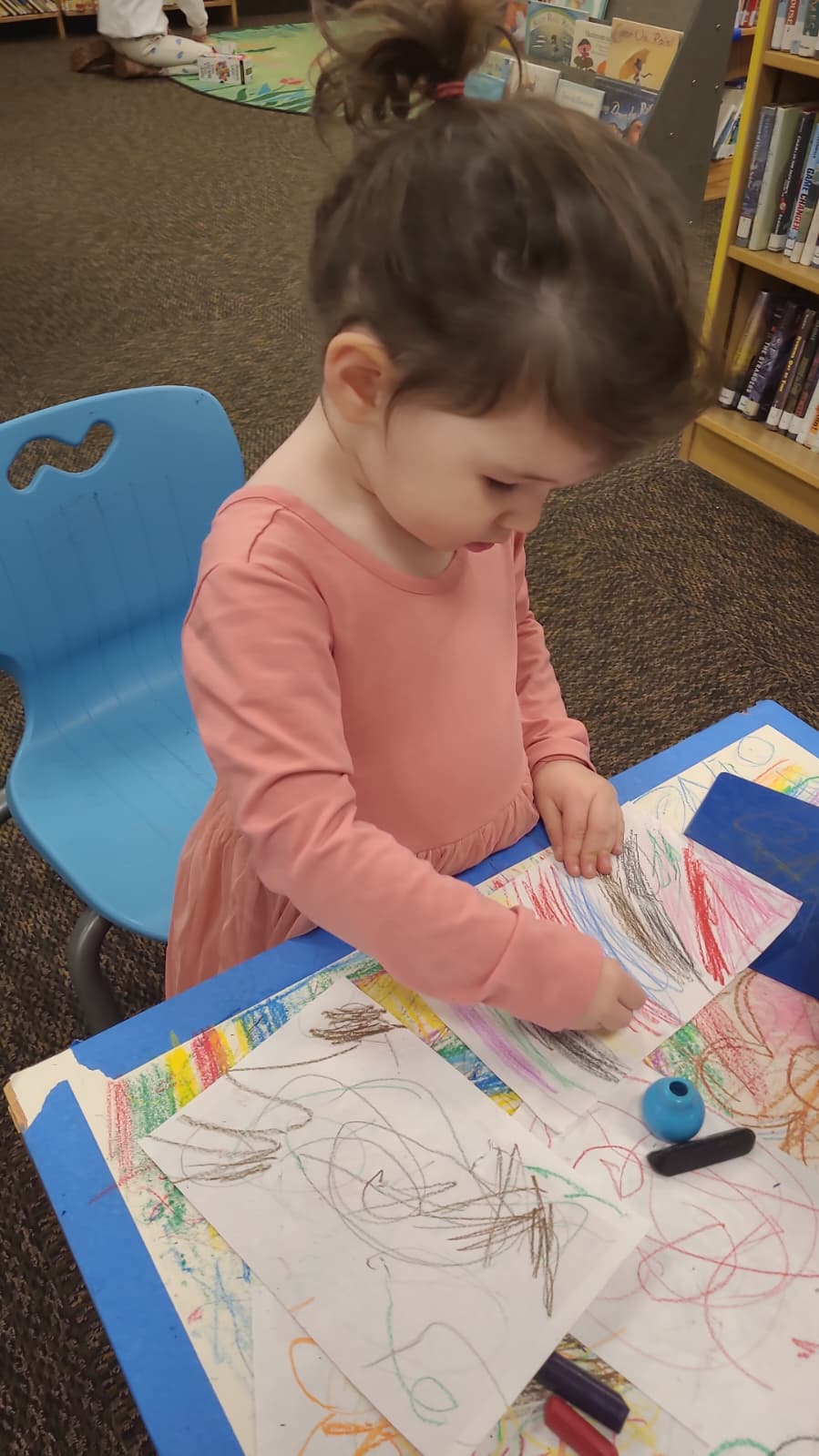 confident Child drawing on her own at a table with art supplies in a classroom setting